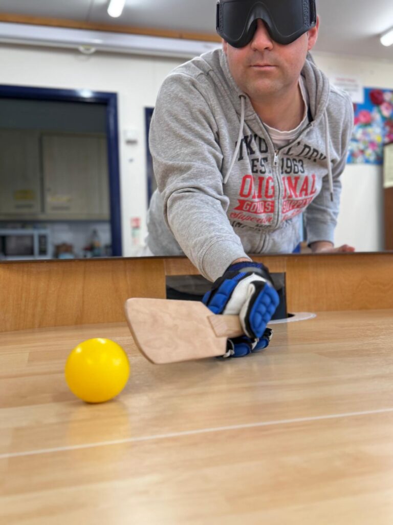 A blindfolded player of showdown reaches for a yellow ball with a bat